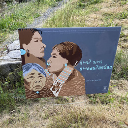 A yard sign with the image of three Native American people and text in a Native language