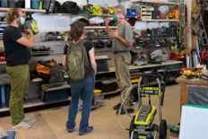 Two volunteers at a tool library help a customer find a tool