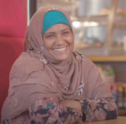 A woman in a hijab sitting at a table in a restaurant, smiling