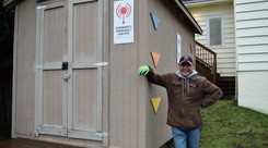 A man smiling and leaning up against a shed with a sign reading "Community Emergency Hub Site"