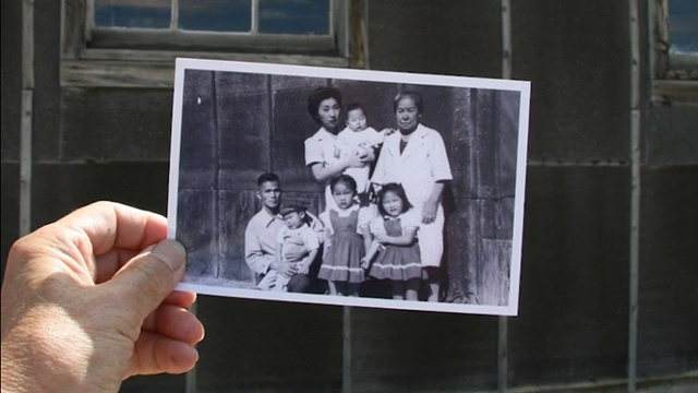 Eugene Tagawa holds a black and white photo of his family at Minidoka