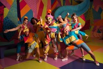 Cherdonna Shinatra surrounded by six individuals dressed in pastel clothing