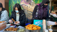 Two volunteers serving food outside of a restaurant with a turtle mural on the wall behind them.