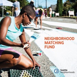 A person kneeling down and holding a paintbrush with text that says "Neighborhood Matching Fund"