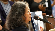 Filipino woman, Teresita Batayola speaking into a microphone at an event.