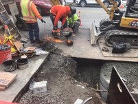 Construction workers using a saw to cut a large metal pipe in the street. 
