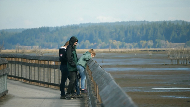 People standing on a boardwalk look out into Puget Sound