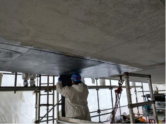 Crews on the work platforms apply carbon-fiber to the exterior of the bridge. 
