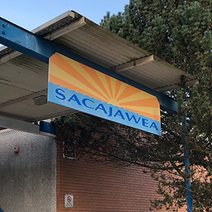 A blue sign with yellow sun rays hanging over a walk-way that says "Sacajawea"