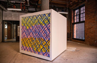 A large, cube shaped art installation stands in a room large vacant room 