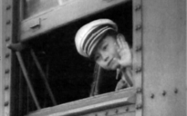 A young Japanese boy wearing a hat, waving from a window