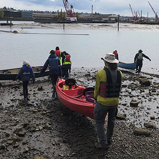A group of people moving canoes along the waterfront of the Duwamish River
