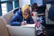 A woman wearing a hijab is sitting on a couch filling out paperwork.