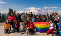 A group of hikers pose holding a Pride flag with Mount Rainier in the background.