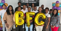 A group of Black people ranging in age standing together and holding gold balloons of the letters B, F, and C. 