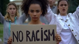 Young black woman holds a sign reading No Racism at a protest rally
