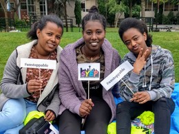 Three Black teenage girls smile for the camera and hold signs promoting SYEP and #unstoppable at the 2019 Capstone event