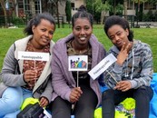 Three Black teenage girls smile for the camera and hold signs promoting SYEP and #unstoppable at the 2019 Capstone event