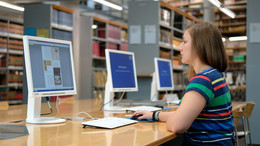 white woman sitting at a computer in a library