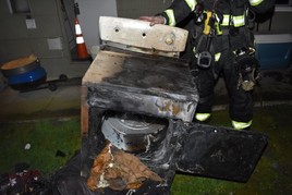 picture of burned clothes dryer with firefighter behind it