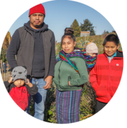 A father, mother, and three children from Guatemala stand in a community garden with the Seattle skyline in the background.