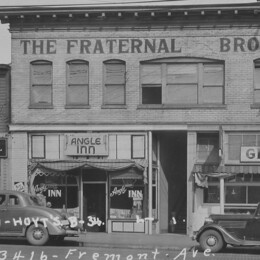 A vintage photo of a brick building exterior with older model cars parked in front. 