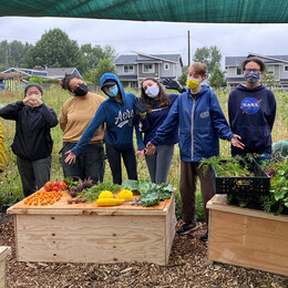 A group of youth standing in behind a display of freshly harvested garden produce.