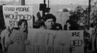 A vintage black and white photo of Asian Americans holding signs at a protest supporting Wounded Knee.