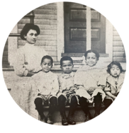 A vintage black and white photo of a Filipino woman and four mixed race Black-Filipino children sitting on a porch. 