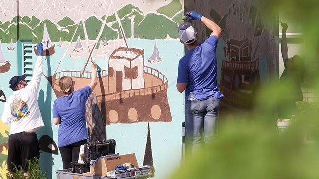 Volunteers touch up a mural