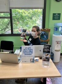 A volunteer research assistant holds up a brochure while sitting at a table at Uplift Northwest