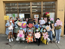 A group of people wearing masks pose with paper flower decorations at an event in the Chinatown-International District