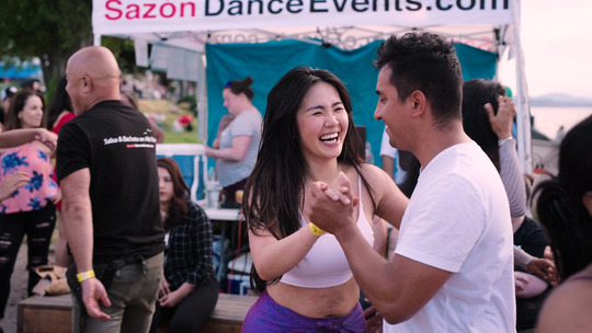 Man and woman from waist up, salsa dancing, woman smiles