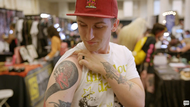 Person in white shirt and red hat rolls up sleeve showing black and red dragon tattoo