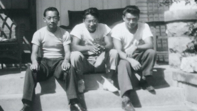 Black and white image of three Asian American men sitting next to each other, dark pants, white t-shirts