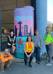 Group of people standing near a tall rain tank with artwork and the words "Water is Life"