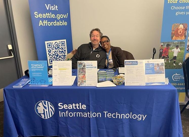 photo of a black woman and a white man sitting at a table with a tablecloth that reads Seattle Information Technology