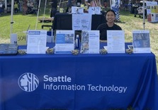 Photo of Asian woman sitting at a table with a table cloth labeled Seattle Information Technology