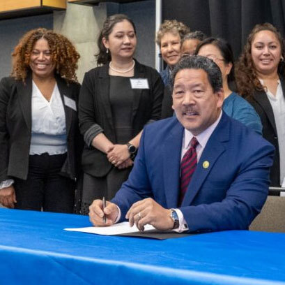 Mayor Harrell signs a bill with people smiling behind.