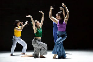 Four dancers in various poses with both arms raised.