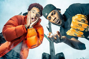 Two Black men pose above the camera, leaning in and down.