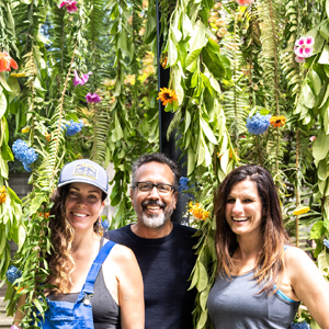 three smiling people standing in a leaf and flower sculpture