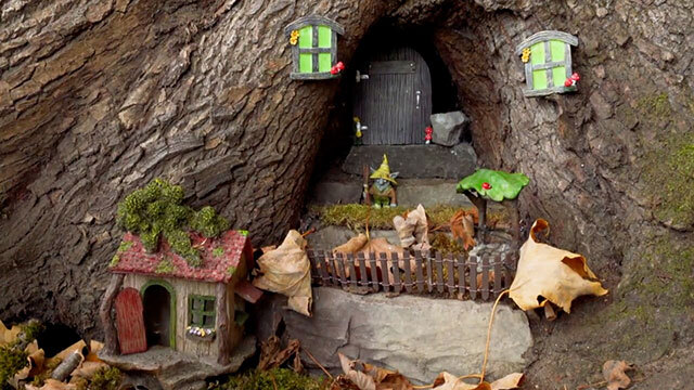 Miniature house, door, windows, fence and gnome placed at base of tree