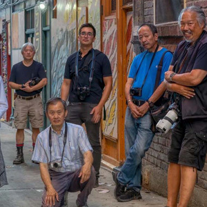 Group of people wearing cameras around their necks leaning against the brick walls in a Chinatown alley looking cool.