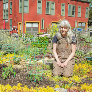 A woman kneeling in her vibrant green, orange and yellow P-Patch surrounding by colorful townhouses.