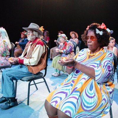 Group of adults sitting on stage dressed up and doing a performance.