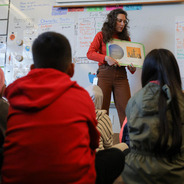 Teacher reading a book to a group of middle school-aged kids.