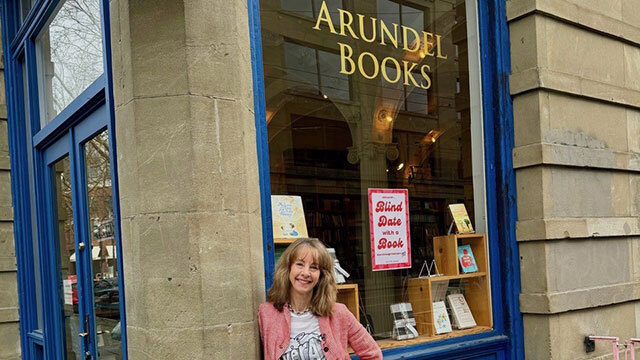 Nancy Guppy leans against outside of Arundel Books with large window behind