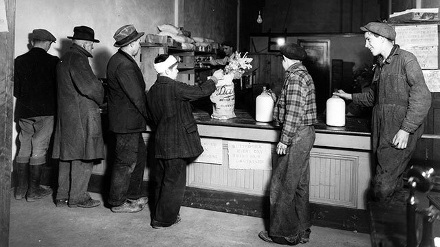 Black and white photo of men and boy lining up at counter for food bags