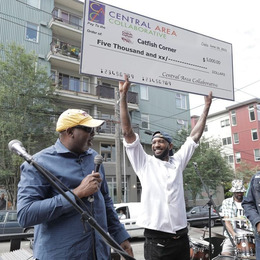 A Black man smiling and holding up an oversized check made out to Catfish Corner